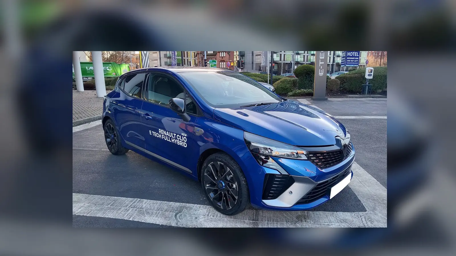 Une Renault Clio bleue photographiée au téléphone sur le parking d'une concession