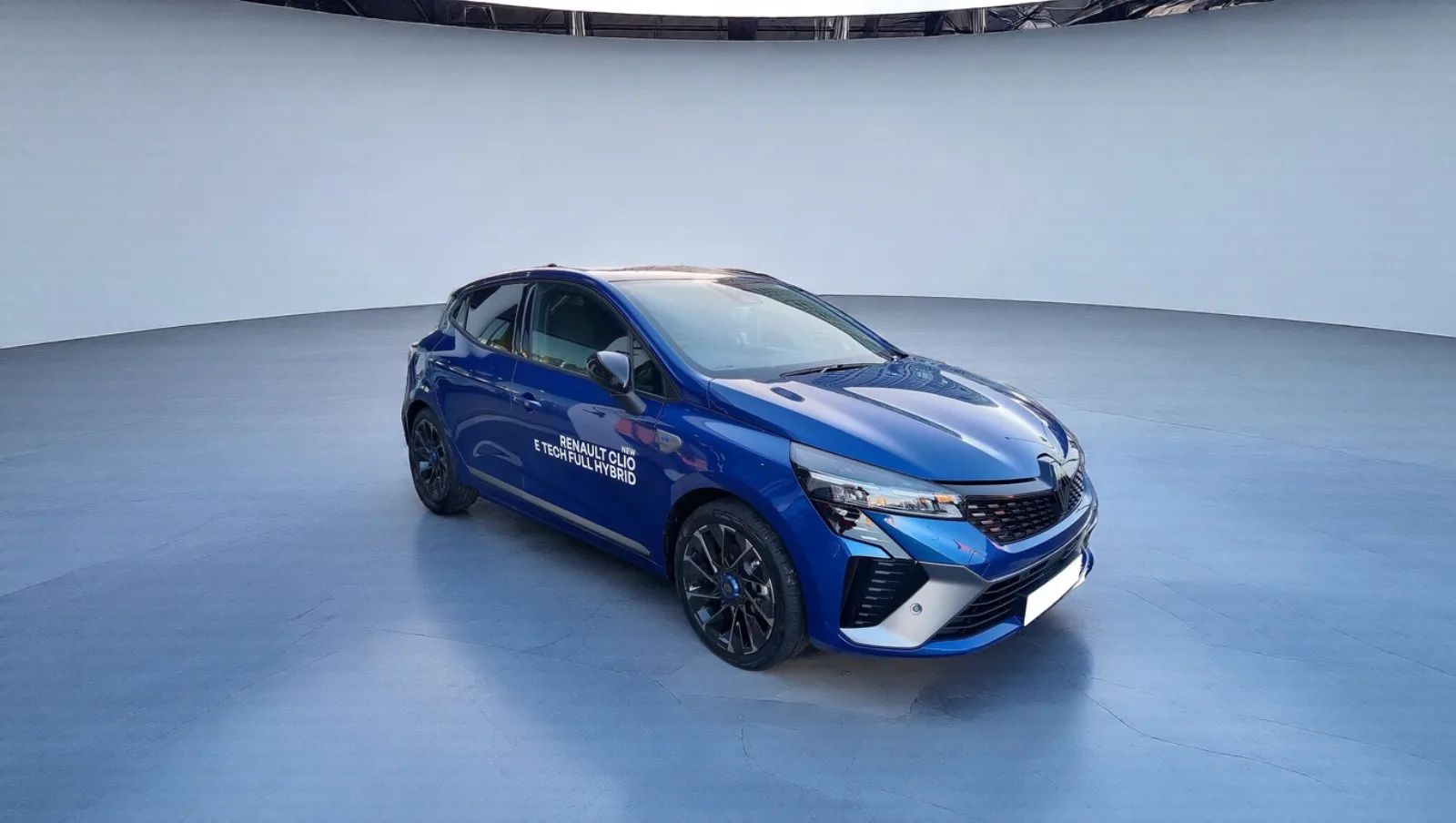 Une Renault Clio bleue photographiée sur un parking, replacée dans un studio gris clair